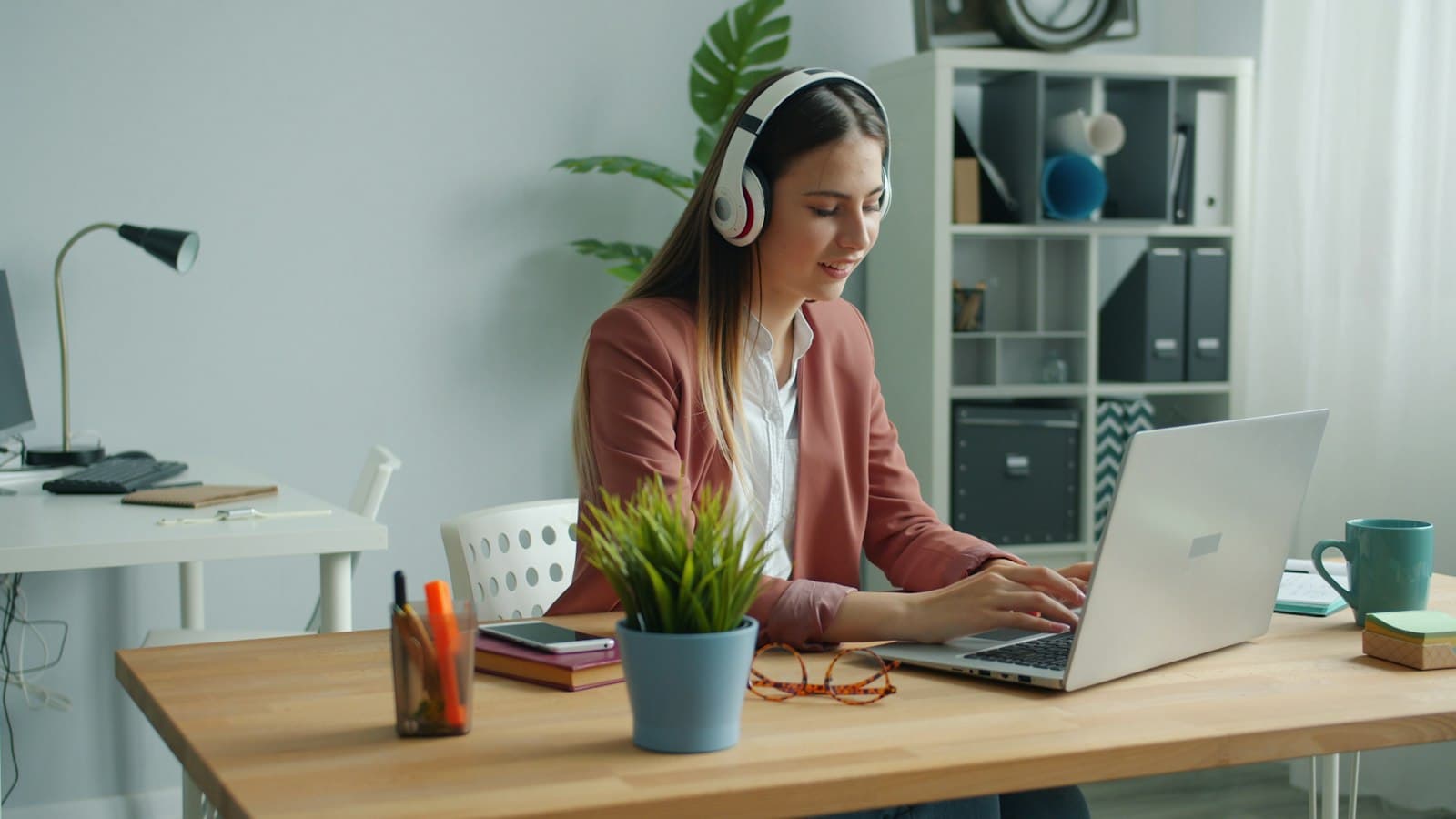 A young woman wearing headphones working on a laptop at her desk.