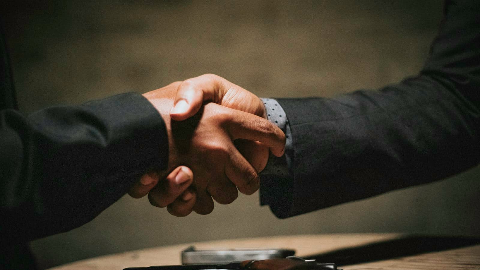 Two people shaking hands over a wooden table.