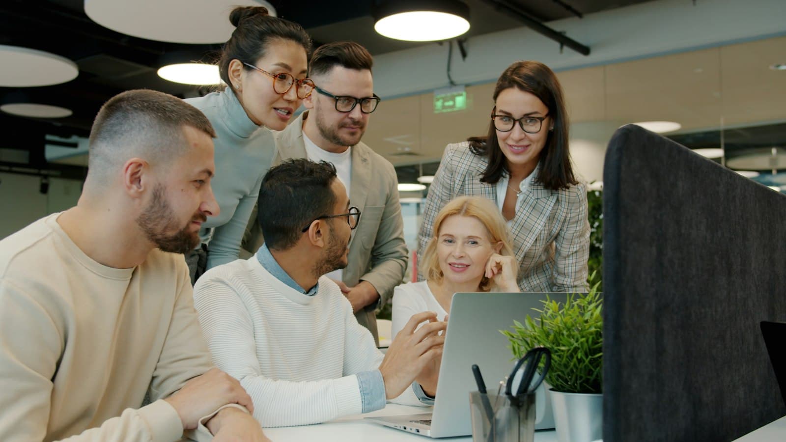 A small team of colleagues gathered around a laptop in an office, discussing what is on the screen.
