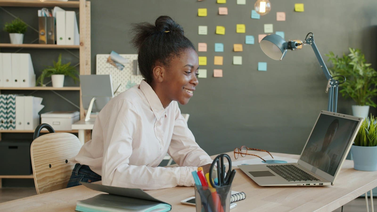 A young professional smiling while working on a laptop at her desk.